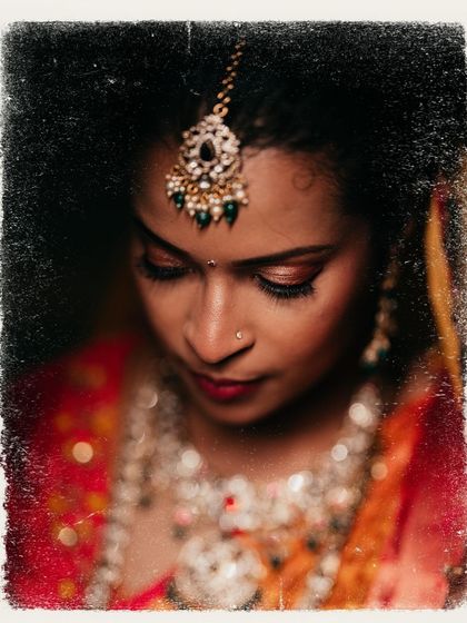 An artistic, textured portrait of a bride, focusing on the intricate details of her maang tikka.