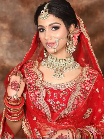 A three-quarter profile of a bride in red, showing off her soft makeup and the floral details in her hair bun.