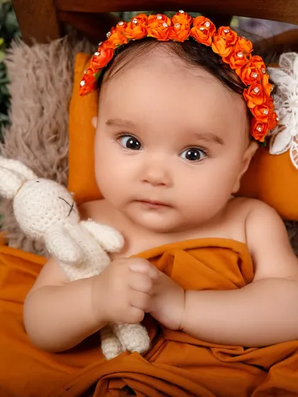 A curious newborn holds a small crochet bunny, looking directly into the camera with her big, beautiful eyes.
