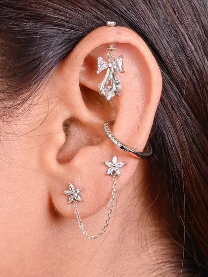 A sophisticated ear curation featuring a delicate angel wing hanging, a conch hoop, and a double star stud connected by a fine chain. This look is all about intricate details.