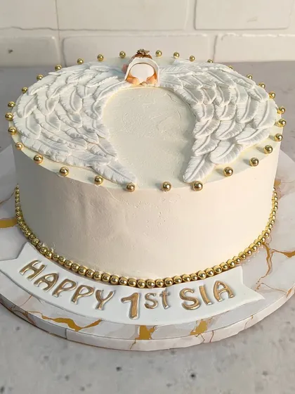 A heavenly cake for a first birthday. This design features beautiful, handcrafted angel wings and a delicate halo, all finished with gold pearl details for a touch of elegance.
