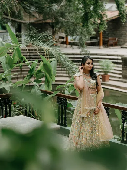 A bride in a light green lehenga stands by the pond, the natural setting enhancing her beauty.