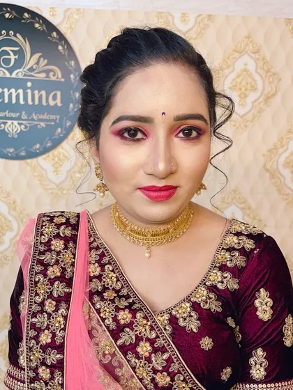 A beautiful engagement or reception look. The makeup features pink and gold tones on the eyes, a bright pink lip, and a simple updo that complements her heavily embroidered velvet blouse.