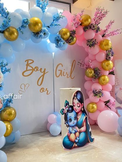 An angled view of the Krishna-Radha themed gender reveal party, showing the depth of the balloon arches and the placement of the character cutouts.