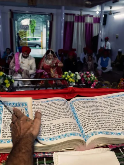 A powerful image capturing the Anand Karaj from the perspective of the Granthi reading the holy Guru Granth Sahib. This unique angle emphasizes the spiritual foundation of the Sikh wedding ceremony.