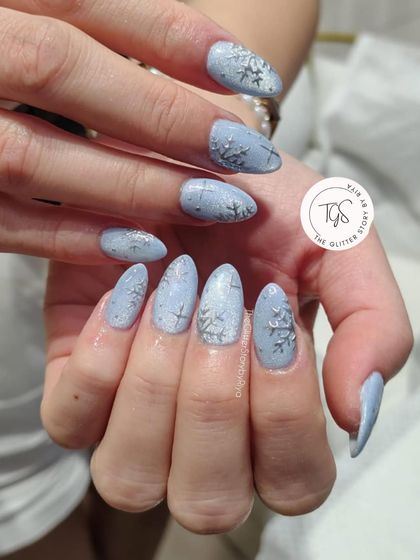 A perfect winter manicure featuring a frosty light blue base with delicate, hand-painted silver snowflakes. The textured finish gives the look of freshly fallen snow.