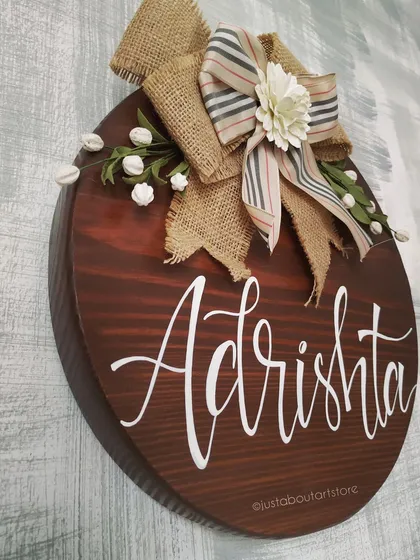 A duplicate of 218, a side angle of the "Adrishta" name plaque, showing its thickness and the rich texture of the wood grain and burlap bow.