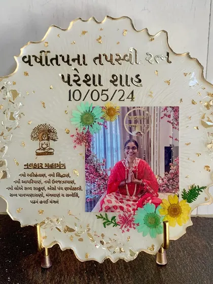 A bright and colorful frame celebrating a religious milestone, with a photo, mantra, and preserved flowers against a yellow background.