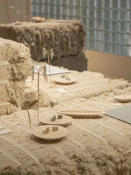 A close-up of the jewelry display on the raw cotton bales. The soft, organic texture of the cotton provides a beautiful backdrop for the metallic forms of the jewelry, highlighting their precision and craft.