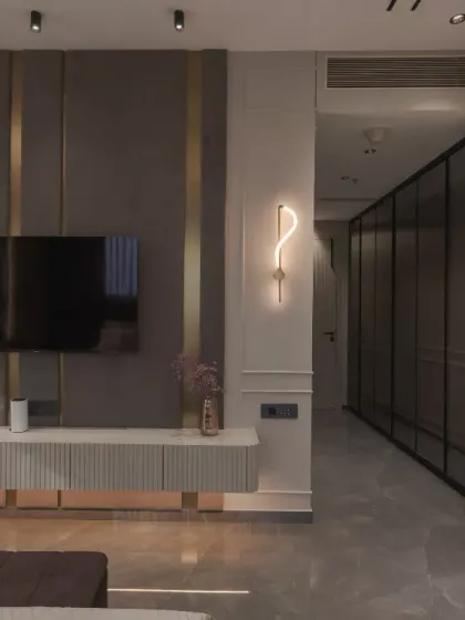 This bedroom space exudes modern elegance with its bespoke design. The fabric paneling, accentuated by gold trims, creates a rich backdrop for the floating console and sleek TV unit, optimizing vertical space.