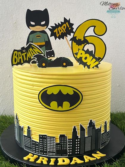 "I am Batman!" This striking Batman cake features the iconic Gotham City skyline and Bat-Signal. The bold yellow and black design, made with whipped cream and edible toppers, is perfect for a young superhero's celebration.