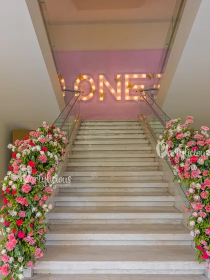 A grand staircase decorated with lush floral arrangements and marquee lights spelling 'ONE', making for a spectacular entrance.