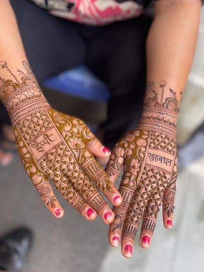 A beautiful Raksha Bandhan design. One hand has 'Bhai' written, and the other has 'Raksha Bandhan', surrounded by intricate floral and jaali patterns.