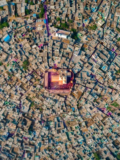 A top-down aerial photograph of the Holi celebration at Nandgaon temple, with the vibrant colors of the festival contained within the temple courtyard, creating a stunning contrast with the surrounding city.