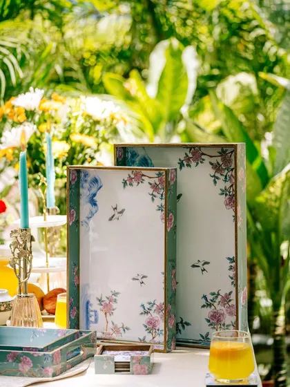 Vigneto's floral-patterned trays and home accessories displayed on a table in a lush garden. This shot seamlessly blends the products with a beautiful, natural environment.