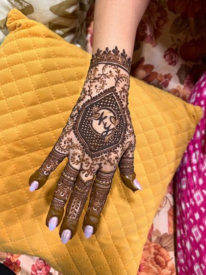 A close-up of a personalized engagement mehendi. The bride's hand features a hexagon with the couple's initials, "K" and "Y", at the center.