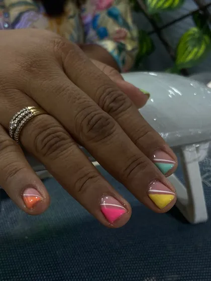 A playful rainbow French manicure on short, natural nails. Each nail features a different pastel color in a geometric tip design, showing how fun and colorful short nails can be.