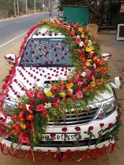 A grand and colorful floral decoration for a white SUV. The design covers the entire front of the car with a dense arrangement of multi-colored flowers.