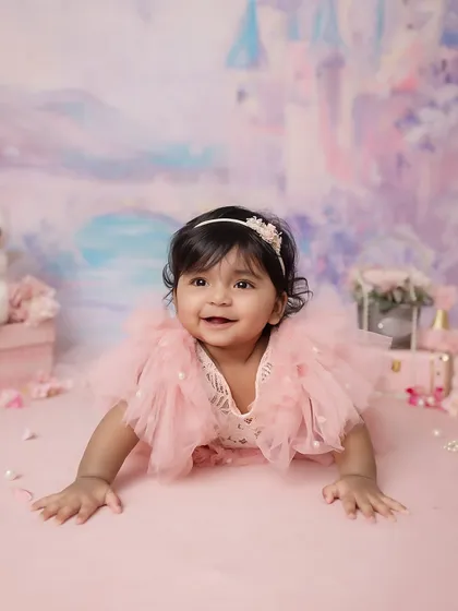 A beautiful 6-month-old baby girl in her princess-themed half-birthday shoot. Her bright smile and the dreamy castle backdrop create a magical portrait.