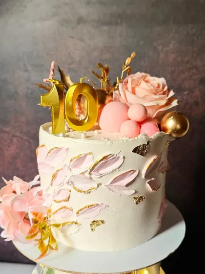 An elegant cake for a 10th birthday, featuring delicate palette-knife painted leaves, fresh flowers, and chocolate spheres in shades of pink and gold.