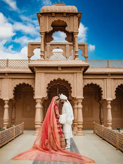 This is the kind of fairytale moment I live to capture. The grandeur of the location is matched only by the love between the couple, with her magnificent red lehenga and trailing veil creating a truly timeless portrait. This is more than a photo; it's the centerpiece of a royal love story.