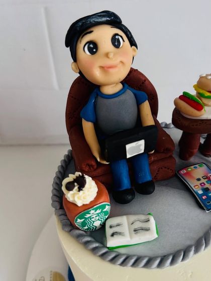 A close-up of the handcrafted fondant figure for a 50th birthday cake, showing him relaxing with his laptop.