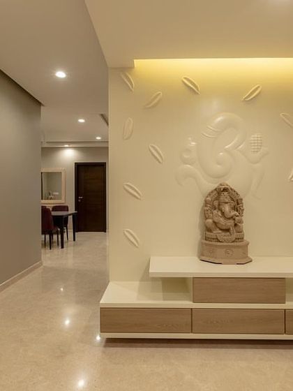 A serene pooja area designed right at the entrance of an apartment. The backdrop features a subtle, 3D Ganesha relief, creating a peaceful and spiritual focal point.