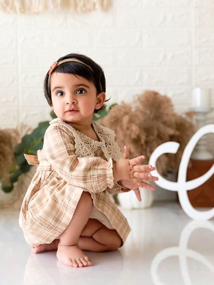 A candid moment from a boho-themed session, capturing the baby in a crouching pose next to the 'One' sign.