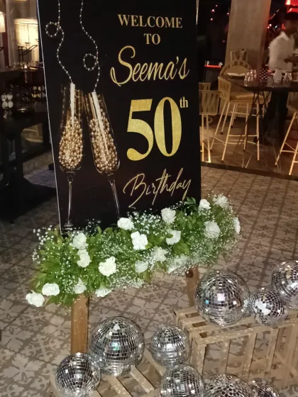 A personalized welcome sign for a 50th birthday party. The elegant black and gold design, paired with fresh flowers and disco balls, sets a glamorous tone.