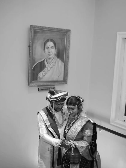 A poignant black and white photo of the couple during their ceremony, with a portrait of an ancestor in the background, symbolizing the blessing of family.