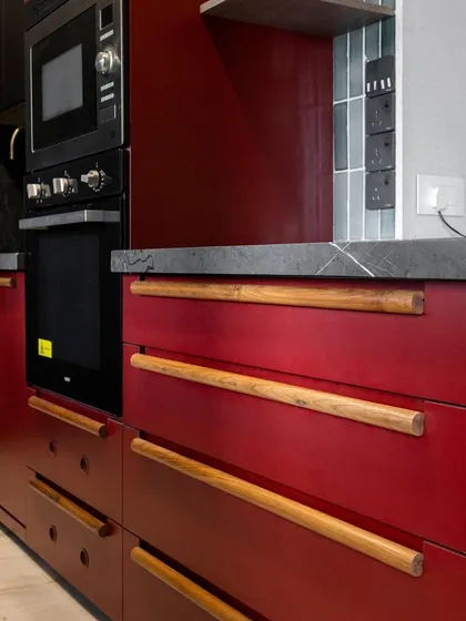 This shot highlights the custom wooden drawer pulls against the Marsala red cabinets. This detail adds a touch of organic warmth and bespoke craftsmanship to the bold color choice.