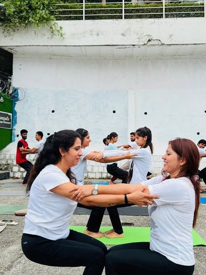 Partner yoga outdoors is a wonderful way to build connection and trust. Here, students support each other in a seated chair pose variation.