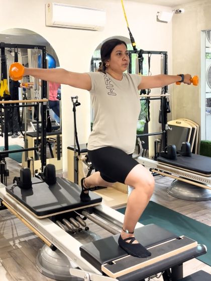 Strong, focused, and in control. This client performs a lunge on the moving Reformer carriage while holding weights, a compound exercise that builds full body strength.