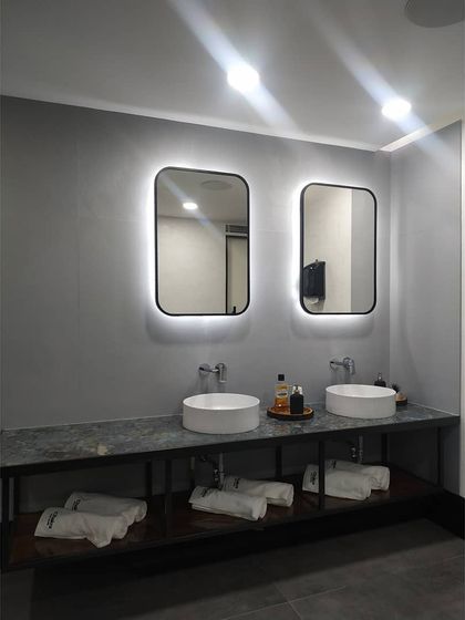 The washroom vanity area, designed for functionality and style. We used vessel sinks, a dark stone countertop, and backlit mirrors to create a clean, modern look that aligns with the studio's premium feel.