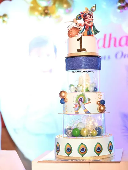 A detailed shot of the Krishna-themed cake, highlighting the peacock feather decorations and the light-up tiers.