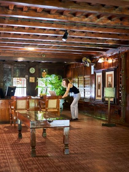 A guest at the reception desk of the Aranmula Palace. The entire space is crafted from dark, polished wood, creating an atmosphere of historic grandeur.