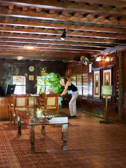 A guest at the reception desk of the Aranmula Palace. The entire space is crafted from dark, seasoned wood, creating a warm and historic ambiance that sets the tone for an authentic Ayurvedic experience.