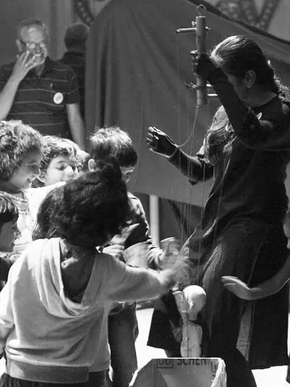 A black and white photo capturing the chaotic, joyful energy of children swarming to play with the puppets after a show.