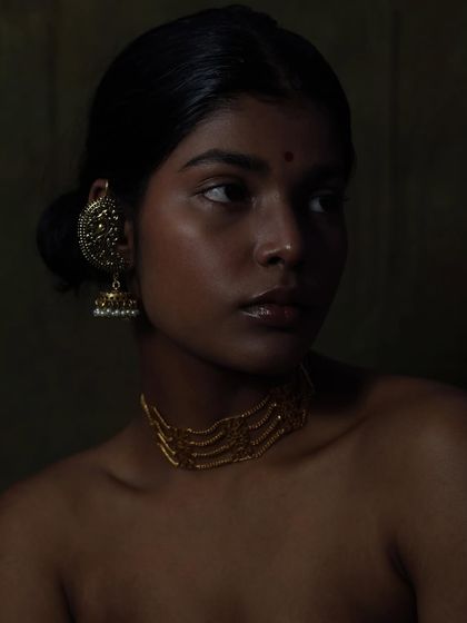 The model's off-camera gaze adds a sense of story and contemplation to this portrait. The lighting remains focused on highlighting the traditional gold jewelry against her rich skin tone.