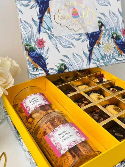 Our signature Diwali hamper is a feast for the senses, presented in a beautifully designed box with a vibrant parrot motif. It's filled with an assortment of our handcrafted treats, including jars of Golden Crunch Medley and Sesame Peri Peri Crackers, alongside brownie bites and granola cups.