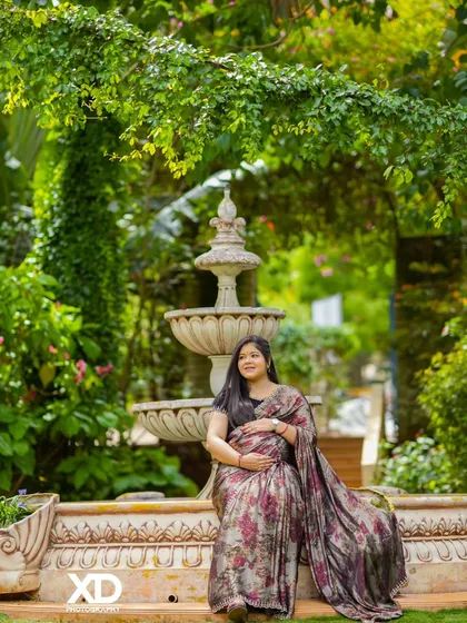 A solo portrait of the mother-to-be seated by a garden fountain, looking peaceful and radiant.