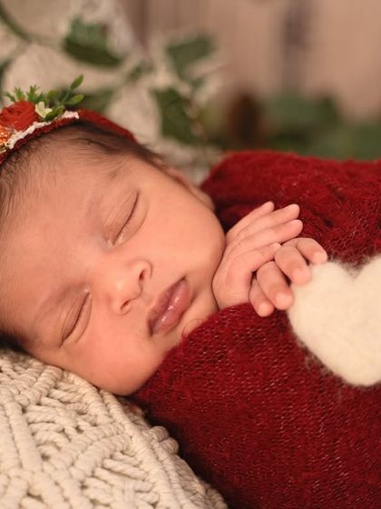 A close-up from the red camper session, showing the baby's peaceful face, a floral headband, and a sweet heart detail on the cozy wrap.
