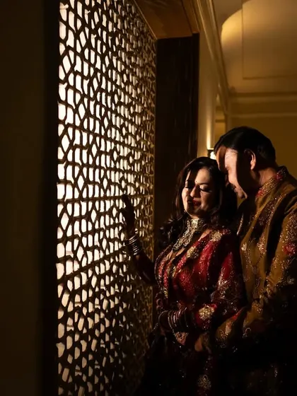 An intimate portrait of the couple by a traditional Rajasthani jali window. The warm, soft lighting creates a romantic and regal atmosphere, perfect for their milestone celebration.