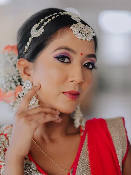 A close-up portrait of a model in a red lehenga, highlighting her dramatic makeup and traditional jewelry. The soft focus creates a dreamy and romantic feel.