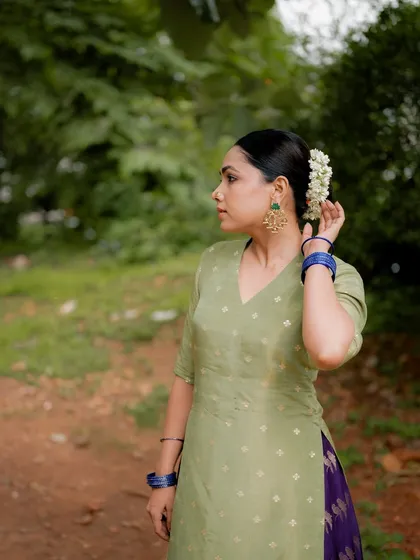 A portrait of actress Anupama Gowda in a simple green kurta, set against a natural background. Her pose and expression convey a sense of calm and grace.