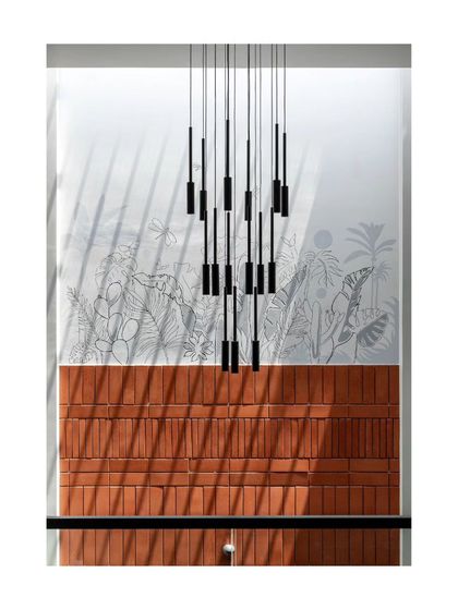 A detail of the '22'x110' House', where a custom light fixture hangs in a double-height space against a backdrop of exposed brick and a delicate wall mural.