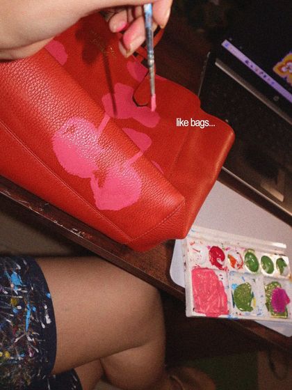 A work-in-progress shot of me painting a floral design on a bright red leather bag. The process starts with laying down the base colors before adding the finer details.