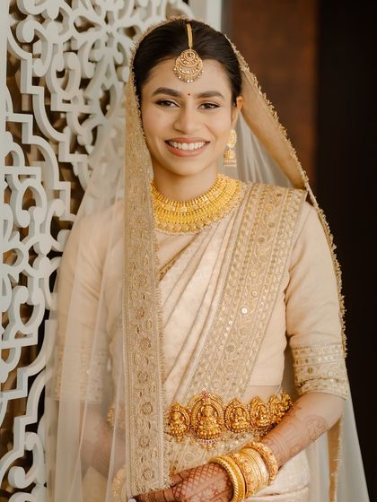 This happy bride showcases a beautiful, minimal South Indian bridal look. The makeup is fresh and light, complementing her stunning gold jewellery.