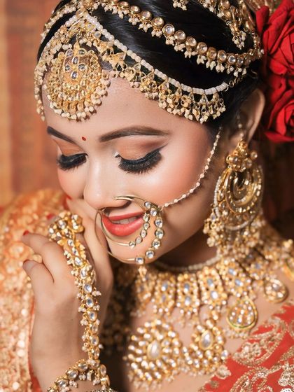A smiling bride showing off her full golden jewellery set, including the intricate hathphool and nath. The red roses in her hair complete the look.