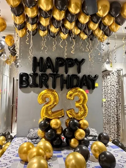 A classic black and gold theme is perfect for a 23rd birthday celebration. This room decoration includes helium balloons on the ceiling, large foil numbers, and balloon bunches on the floor, creating a festive and glamorous atmosphere.